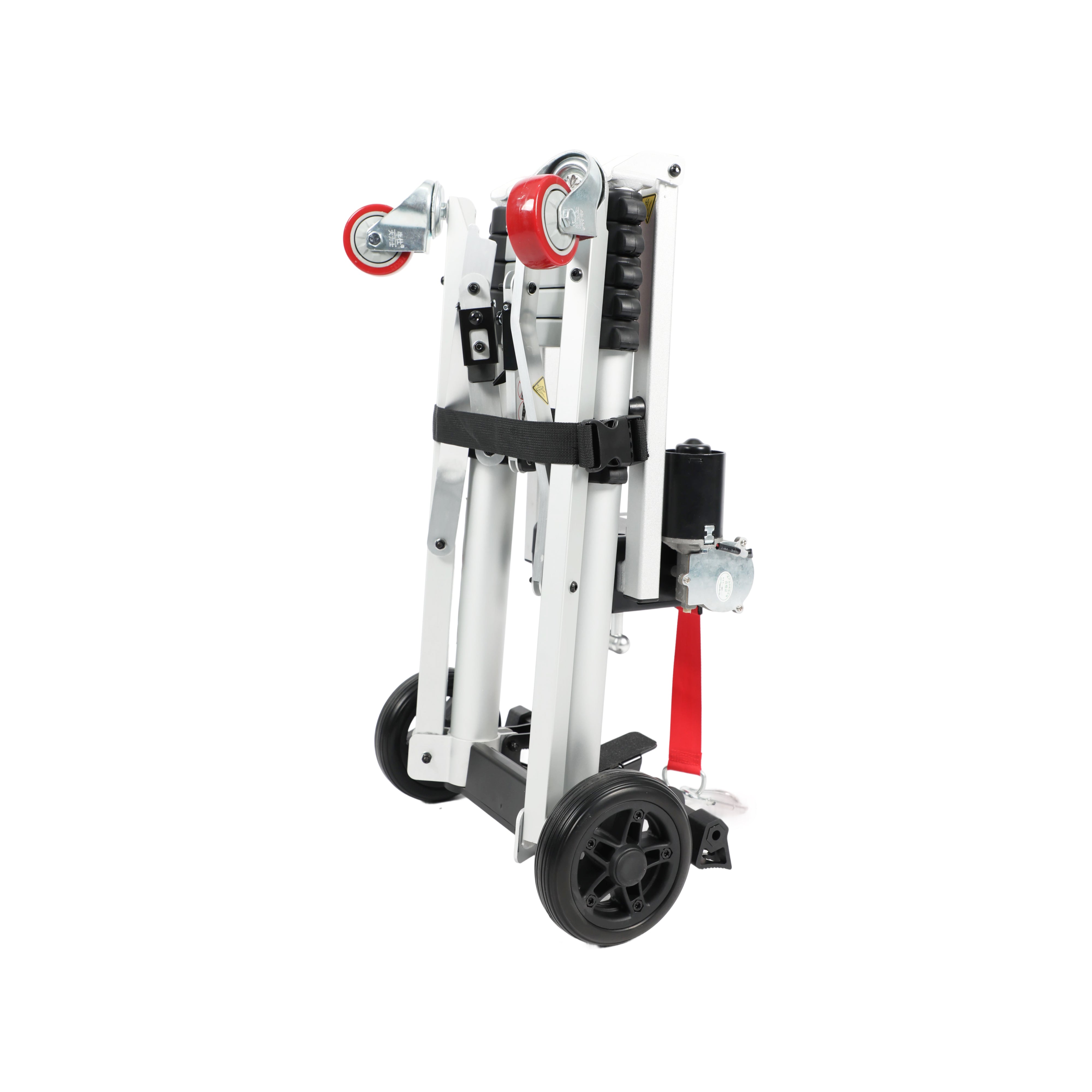 An angled view of the Muvon Mobility portable lift, showing the unit in its folded, transport-ready state. This perspective highlights the two red caster wheels at the top and the heavy-duty black wheels at the base, emphasizing its portability. The silver aluminum telescopic frame is securely bundled with a black adjustable buckle strap, while the motor assembly and a red safety strap are visible on the side.