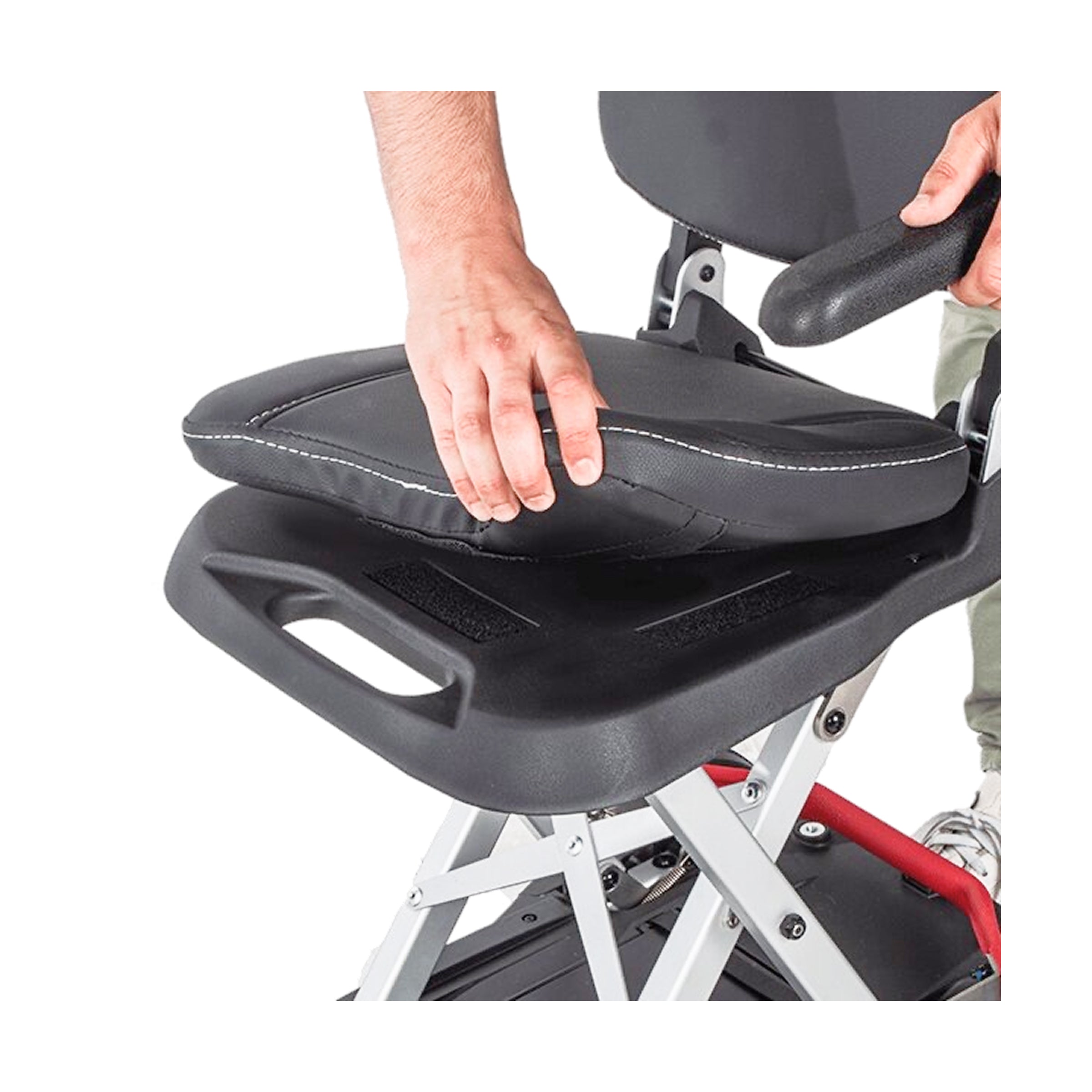 A close-up shot showing a person’s hand lifting the black padded seat cushion away from the Muvon One mobility scooter's frame. The image demonstrates how the cushion is attached, revealing a built-in handle underneath the seat for easier carrying when the scooter is folded.