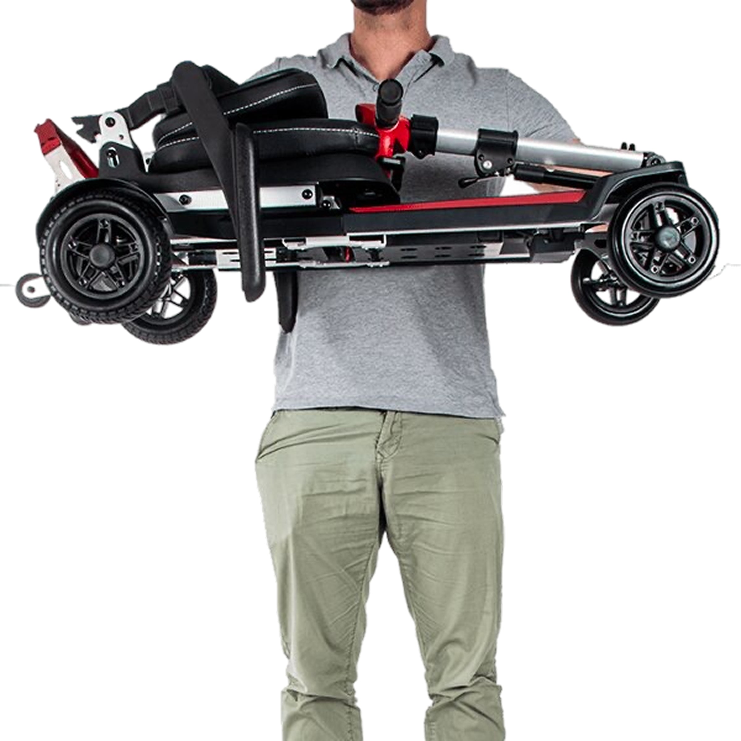 A person holding the Muvon One mobility scooter horizontally with both hands to demonstrate its lightweight design. The scooter is fully folded into a compact, rectangular shape with the red tiller tucked against the black seat and the four wheels visible at the corners.
