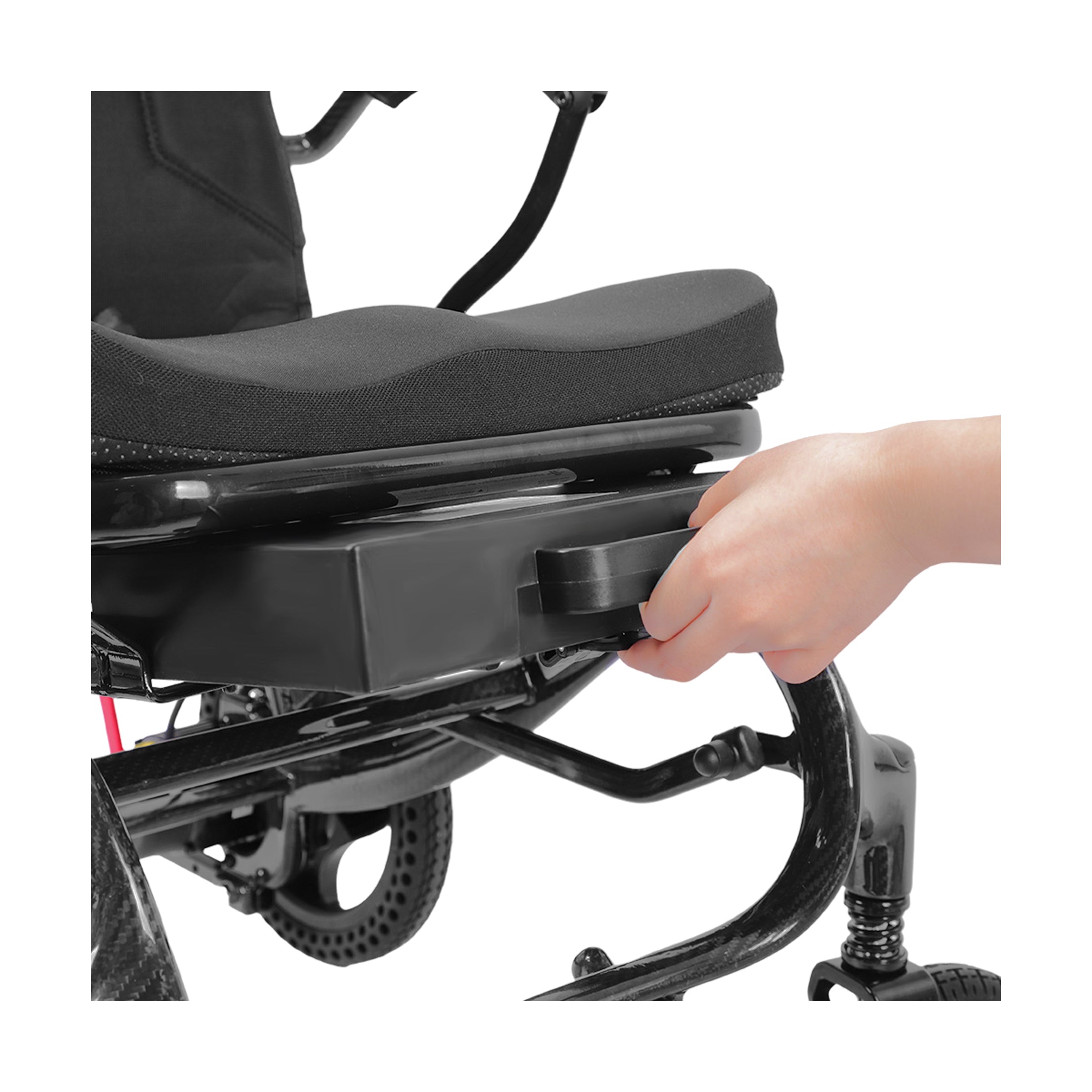 A close-up shot showing a person’s hand sliding a slim, black rectangular battery pack into the dedicated compartment located directly beneath the seat of the Harvey Carbon Power Wheelchair.
