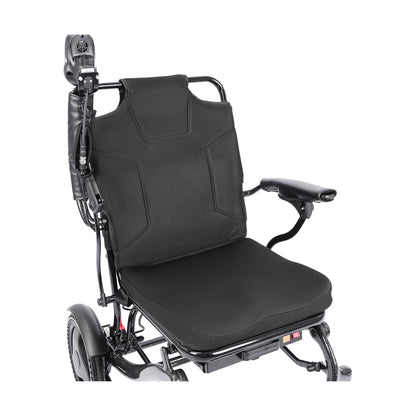 An angled top-down perspective view of the Harvey Carbon Power Wheelchair's seat and backrest. This view emphasizes the plush, black contoured cushion of the seat and backrest. A joystick is mounted on the right armrest, which has a protective sleeve on its base. The carbon fiber texture of the frame and a large drive wheel are visible. Below the seat, a storage pouch and the red power switch can be seen.