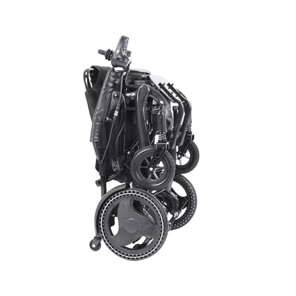 A side view of the Harvey Carbon Power Wheelchair in its completely folded and compact state. The black components are nested together, including the seat and backrest, which are folded up against the main carbon fiber frame. All four wheels (large drive wheels and small casters) are compressed. The joystick controller on its armrest is visible at the top, and the footplate is tucked away, with a small anti-tip wheel on the ground.