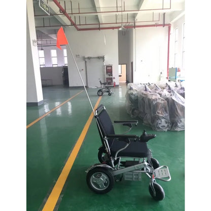 A high-visibility Muvon Mobility safety flag with a bright orange triangular pennant mounted on a tall, flexible pole attached to the rear of an electric wheelchair.