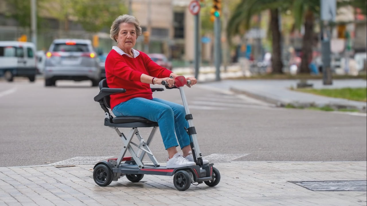Load video: A video of an elderly woman navigating a street with her Muvon One Mobility Scooter. She appears happy and comfortably dressed for an outing in a vibrant red sweater and casual jeans. The Muvon One™ Lightweight Foldable Mobility Scooter is designed for clear, dependable independence. Built for everyday use, it delivers smooth performance, intuitive controls, and compact portability without unnecessary complexity.