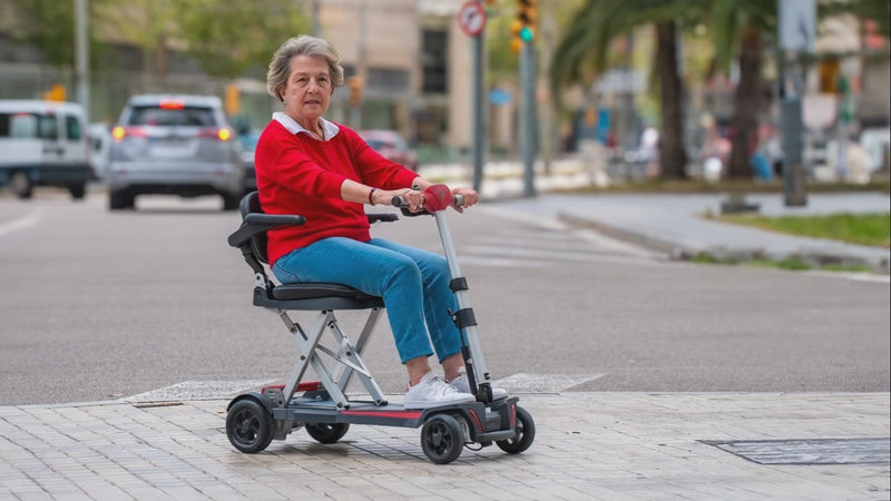 A video of an elderly woman navigating a street with her Muvon One Mobility Scooter. She appears happy and comfortably dressed for an outing in a vibrant red sweater and casual jeans. The Muvon One™ Lightweight Foldable Mobility Scooter is designed for clear, dependable independence. Built for everyday use, it delivers smooth performance, intuitive controls, and compact portability without unnecessary complexity.